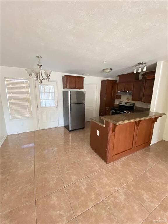 Kitchen with light tile patterned floors, a peninsula, an inviting chandelier, and appliances with stainless steel finishes