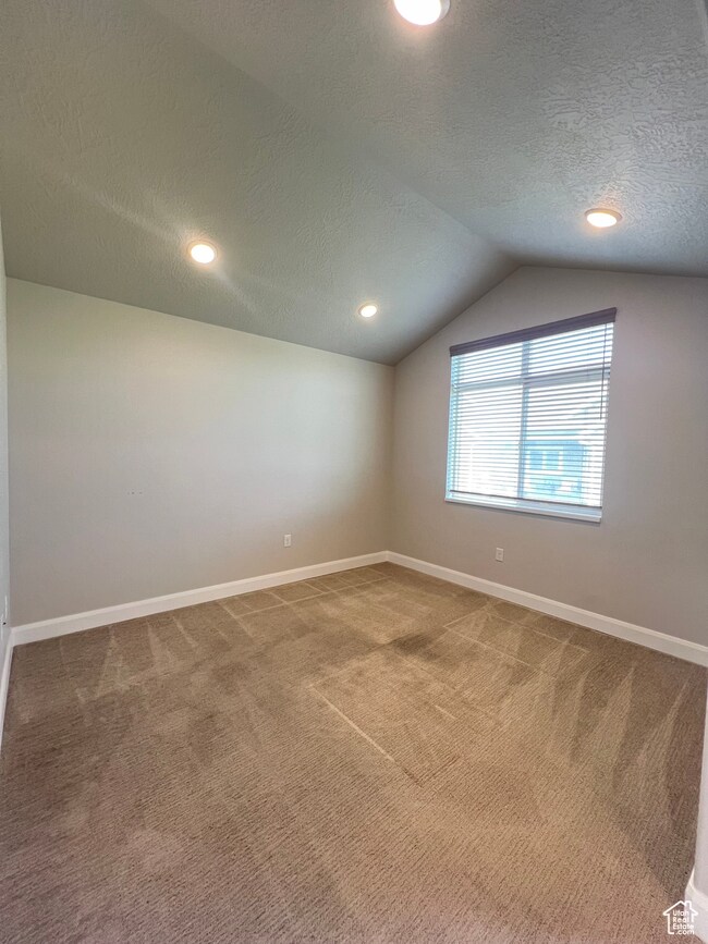 Empty room featuring a textured ceiling, lofted ceiling, light carpet, and recessed lighting