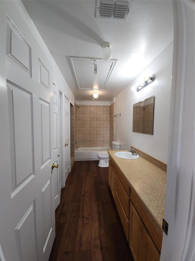 Full bathroom with toilet, vanity,  shower combination, wood finished floors.