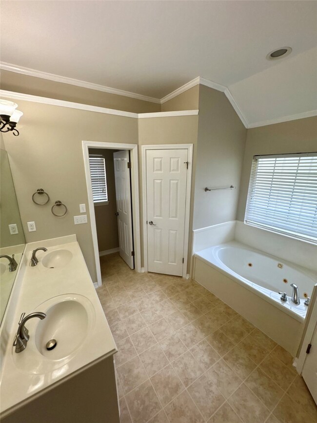 Bathroom with a whirlpool tub, double vanity, ornamental molding, and light tile patterned flooring