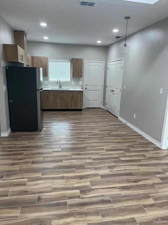 Kitchen featuring freestanding refrigerator, a sink, dark wood-type flooring, light countertops, and baseboards