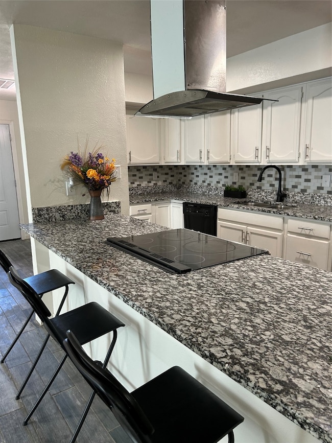 Kitchen featuring a kitchen breakfast bar, white cabinetry, dark stone countertops, and a textured wall