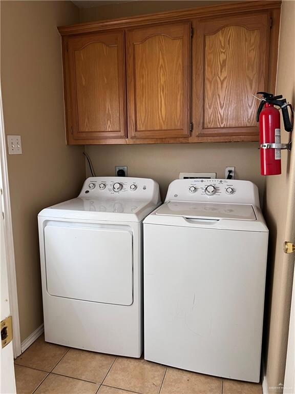 Clothes washing area with washer and clothes dryer, cabinets, and light tile patterned flooring