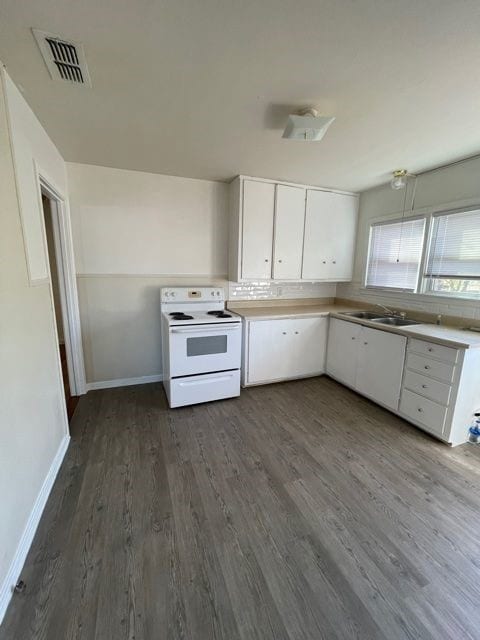 Kitchen with electric range, white cabinets, dark wood finished floors, and light countertops