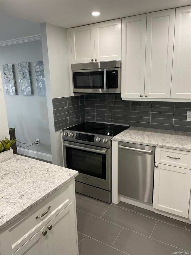 Kitchen with white cabinets, tasteful backsplash, appliances with stainless steel finishes, light stone counters, and ornamental molding