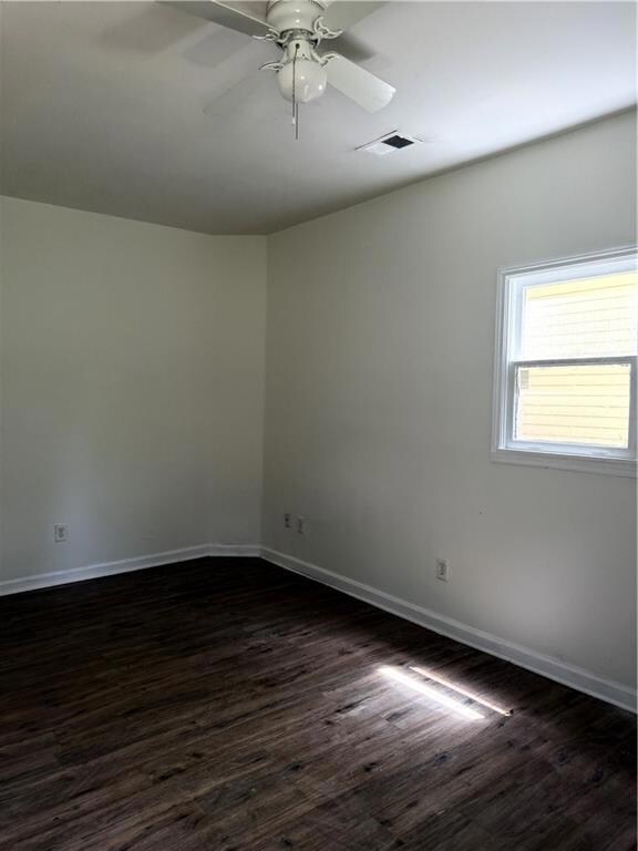 Empty room with dark wood finished floors, baseboards, and a ceiling fan