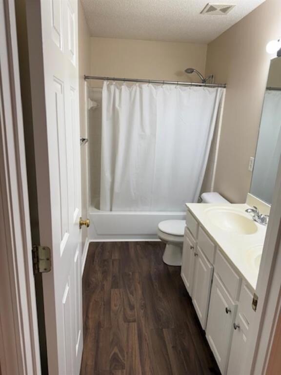 Full bathroom with a textured ceiling, dark wood-type flooring, shower / bathtub combination with curtain, and vanity