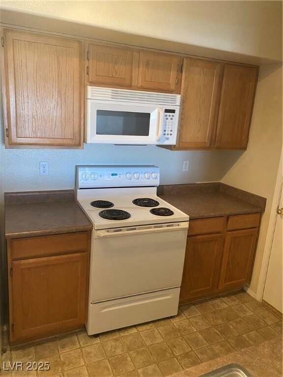 Kitchen with dark countertops, white electric range oven, and brown cabinets