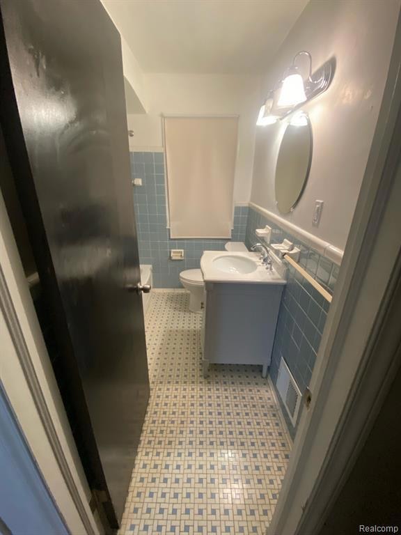 Full bath with tile walls, light tile patterned flooring, vanity, and a wainscoted wall