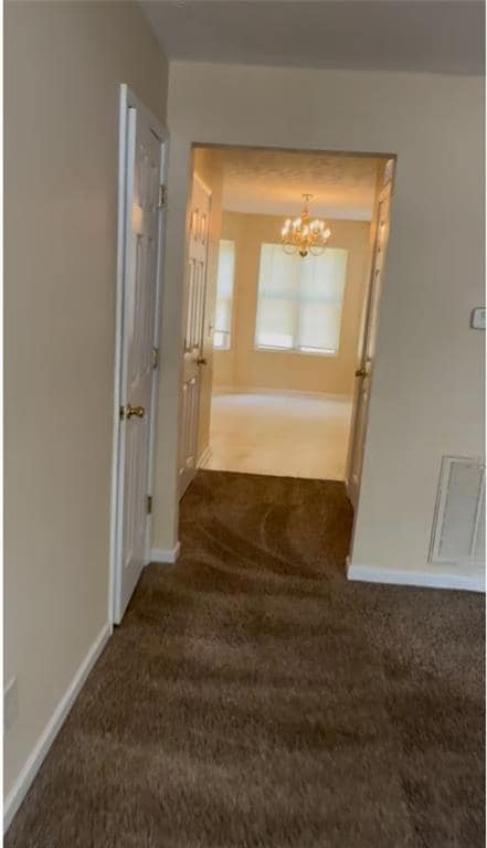 Corridor featuring dark carpet and a chandelier