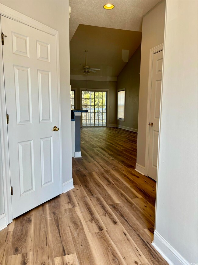 Hall featuring a textured ceiling, wood finished floors, baseboards, and vaulted ceiling