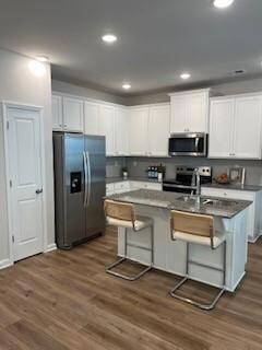 Kitchen with appliances with stainless steel finishes, white cabinetry, a center island with sink, a breakfast bar, and recessed lighting