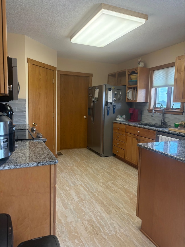 Kitchen featuring dark stone counters, backsplash, brown cabinetry, light wood-style floors, and a textured ceiling