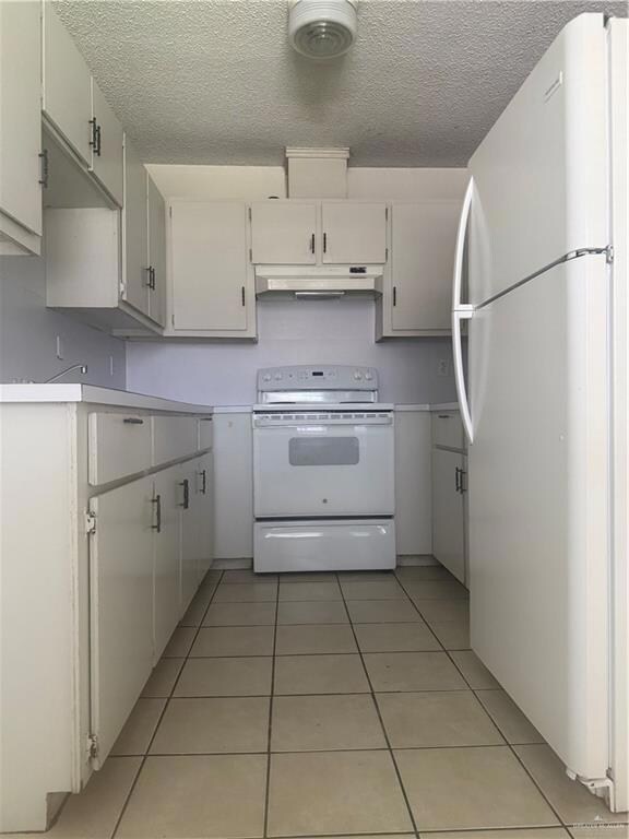 Kitchen featuring fridge, white electric range oven, light tile patterned flooring, a textured ceiling, and light countertops
