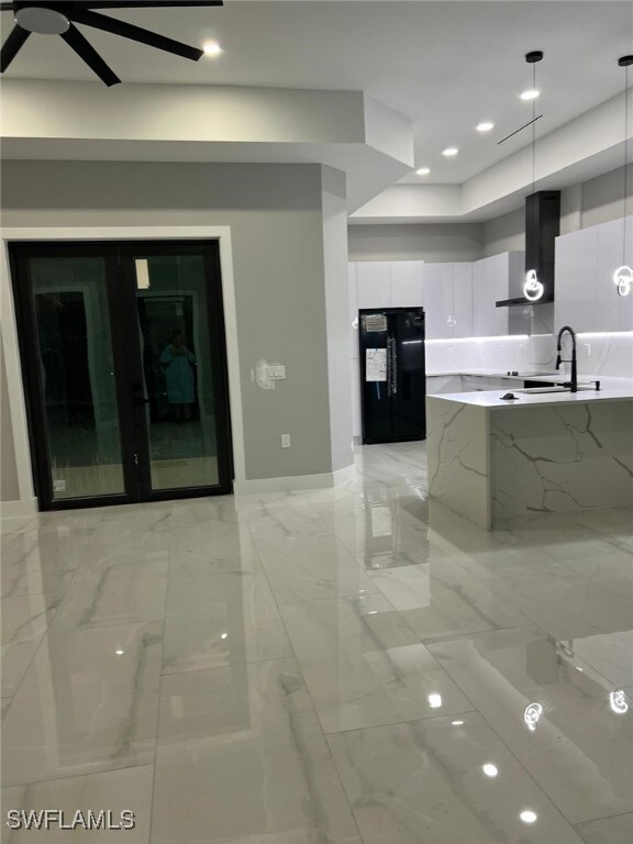 Kitchen with white cabinetry, modern cabinets, hanging light fixtures, freestanding refrigerator, and wall chimney range hood