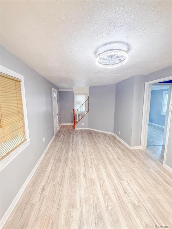 Empty room featuring light wood-style floors, a textured ceiling, and stairway