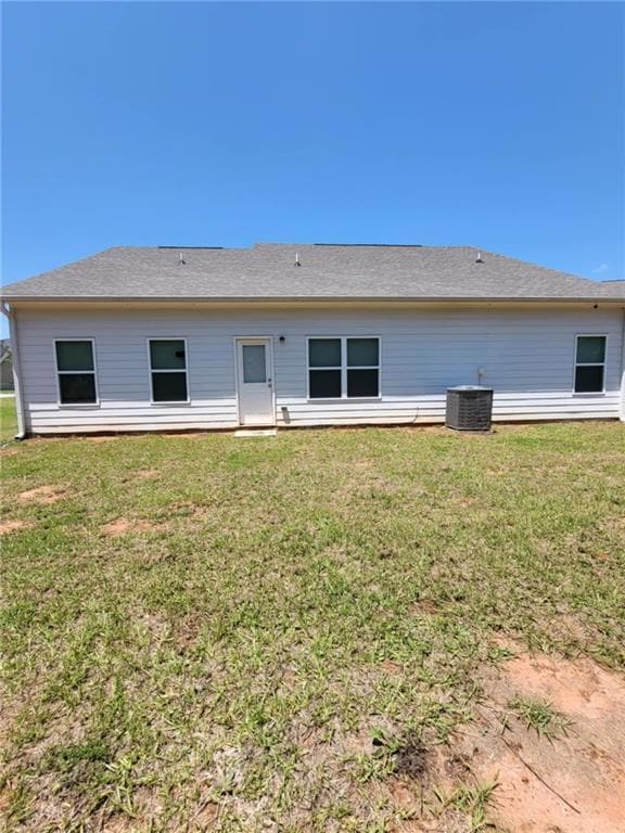 Back of property with central AC unit and a lawn
