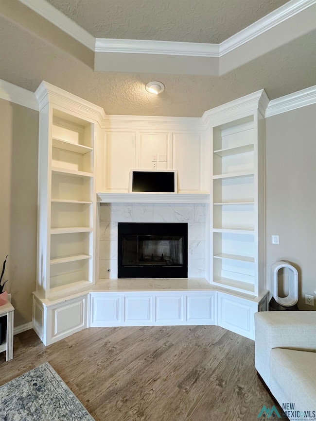 Unfurnished living room with crown molding, wood finished floors, a high end fireplace, and a textured ceiling