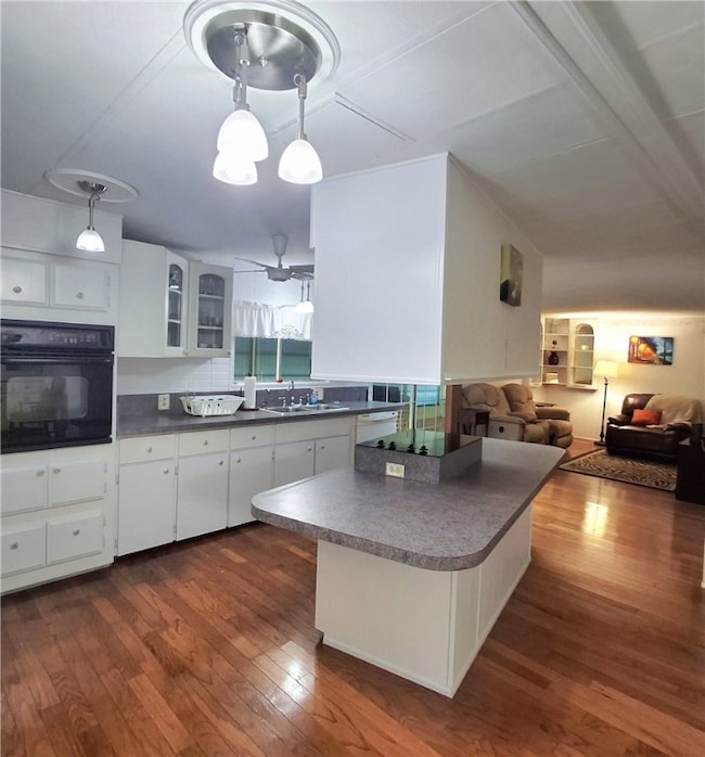 Kitchen featuring white cabinets, black oven, dark wood-style flooring, pendant lighting, and dark countertops