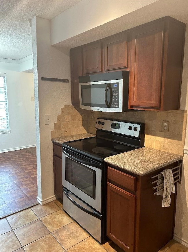 Kitchen featuring stainless steel appliances, decorative backsplash, a textured ceiling, a textured wall, and light stone counters