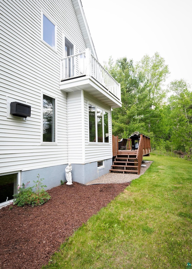 View of side of home featuring a balcony, a yard, and a wooden deck