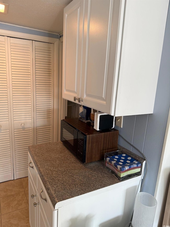 Kitchen featuring white cabinetry, dark countertops, light tile patterned flooring, black microwave, and a textured ceiling