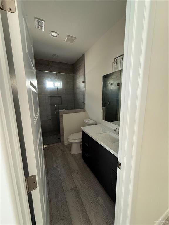 Bathroom featuring wood finished floors, vanity, toilet, a stall shower, and recessed lighting