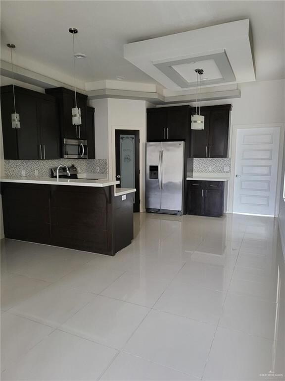 Kitchen featuring light tile patterned flooring, pendant lighting, a raised ceiling, backsplash, and stainless steel appliances