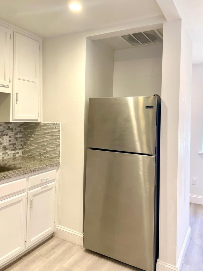Kitchen featuring white cabinetry, freestanding refrigerator, backsplash, light wood-style flooring, and light stone countertops