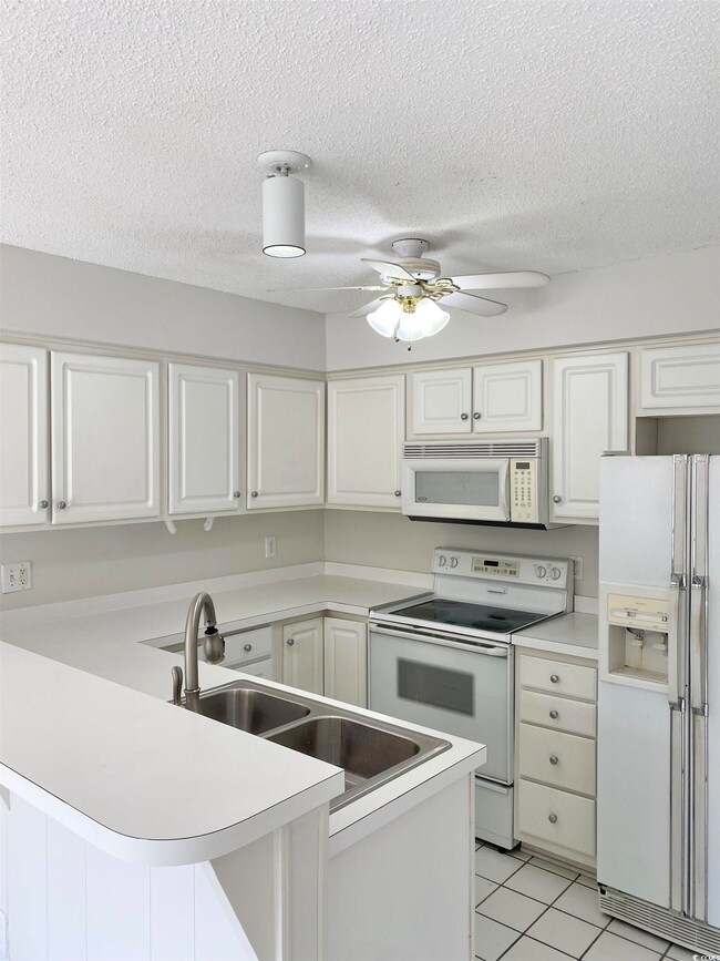 Kitchen featuring white appliances, white cabinetry, light countertops, and a peninsula