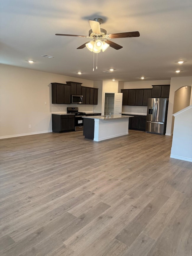 Kitchen with stainless steel appliances, light wood-type flooring, recessed lighting, a ceiling fan, and a kitchen island with sink