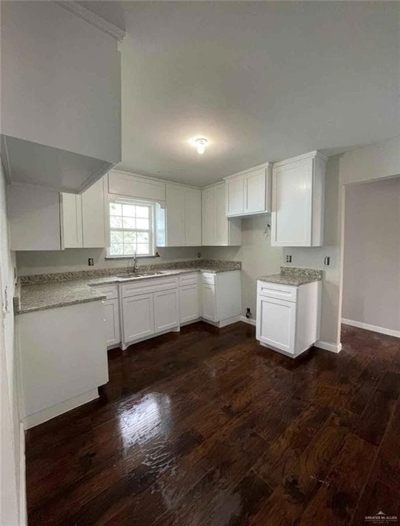 Kitchen featuring dark wood-style floors, white cabinets, a sink, baseboards, and light stone countertops