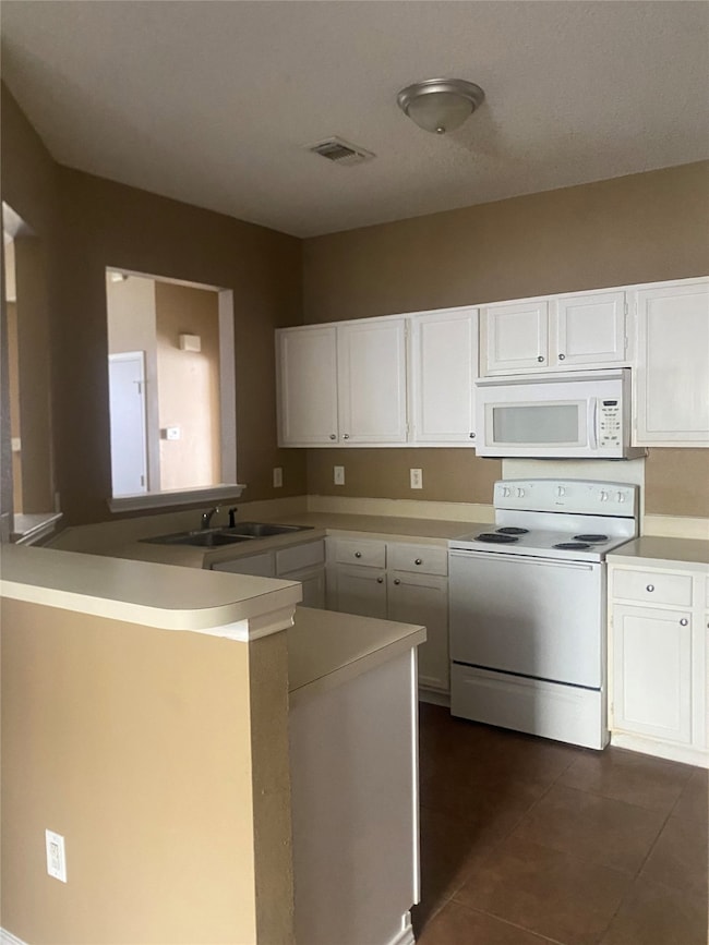 Kitchen with white appliances, a peninsula, white cabinetry, light countertops, and dark tile patterned flooring