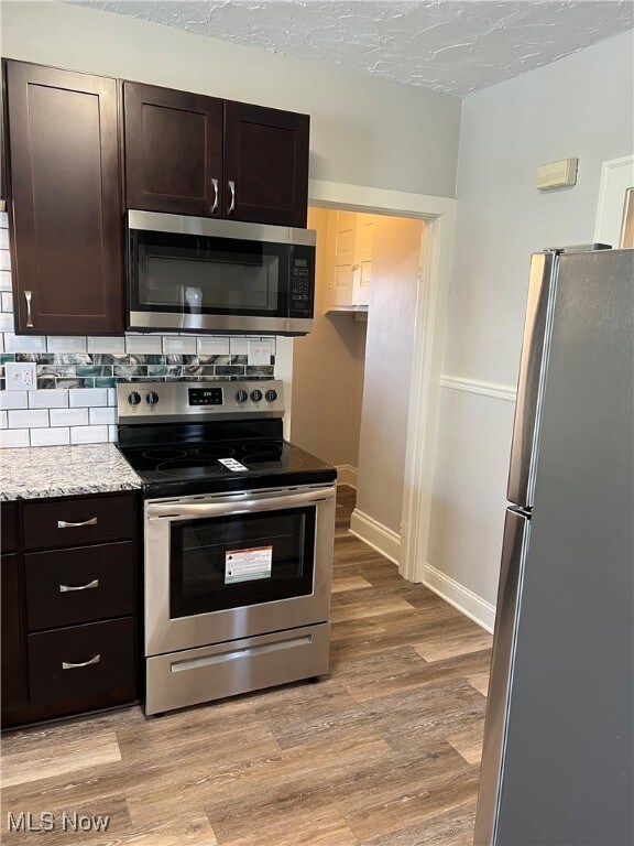Kitchen with backsplash, dark brown cabinets, appliances with stainless steel finishes, light wood-style floors, and a textured ceiling
