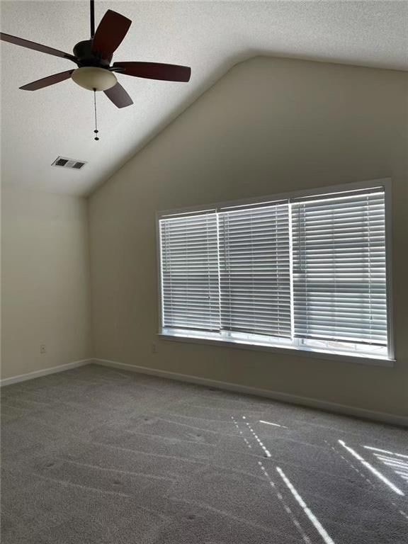 Carpeted spare room featuring ceiling fan, vaulted