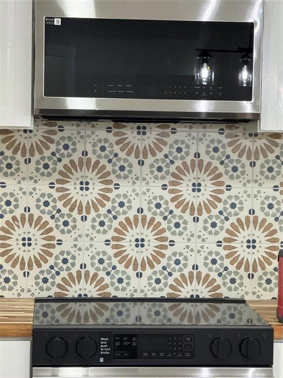 Kitchen view of white cabinetry, stainless steel range, backsplash, and butcher block countertops