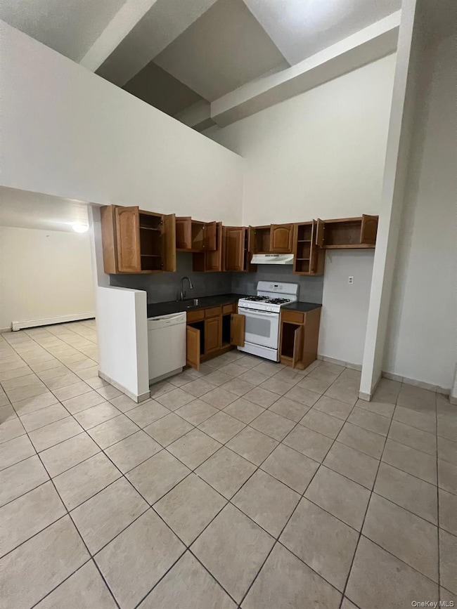 Kitchen with dark countertops, open shelves, light tile patterned flooring, white appliances, and baseboard heating