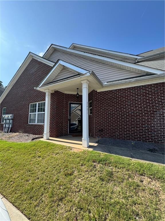 View of property exterior with brick siding, a lawn, and a patio area