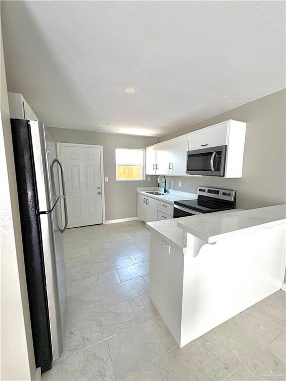 Kitchen featuring appliances with stainless steel finishes, white cabinets, a peninsula, and light stone countertops