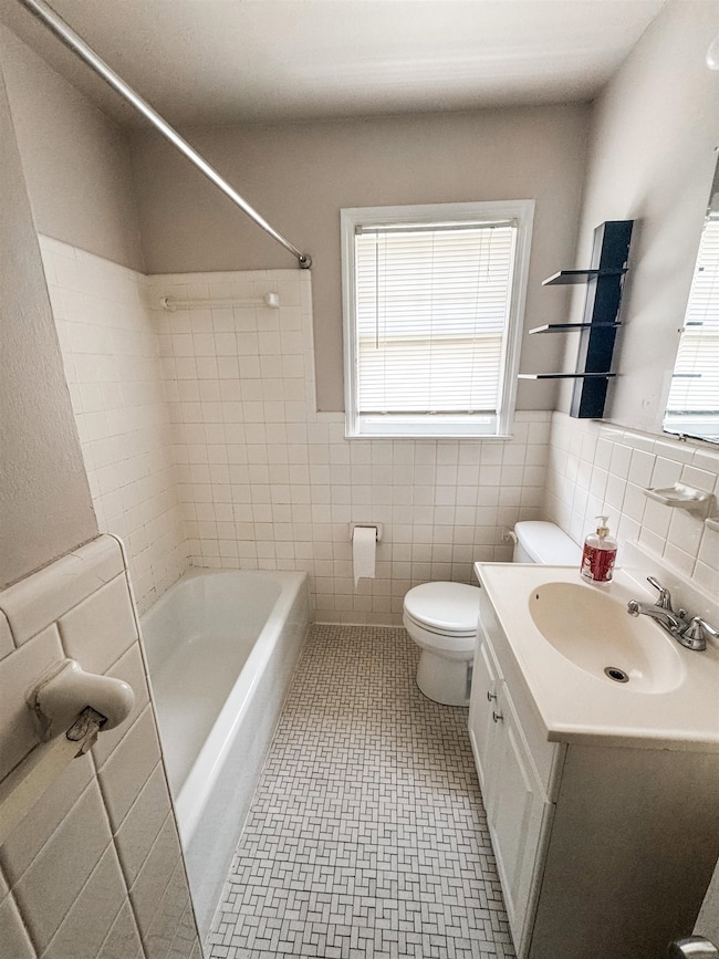 Bathroom featuring vanity, healthy amount of natural light, tile walls, bathtub / shower combination, and wainscoting