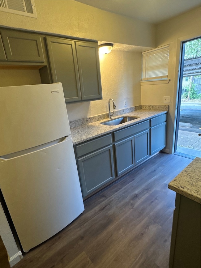 Kitchen with a textured wall, refrigerator, dark wood-style floors, light stone countertops, and gray cabinets