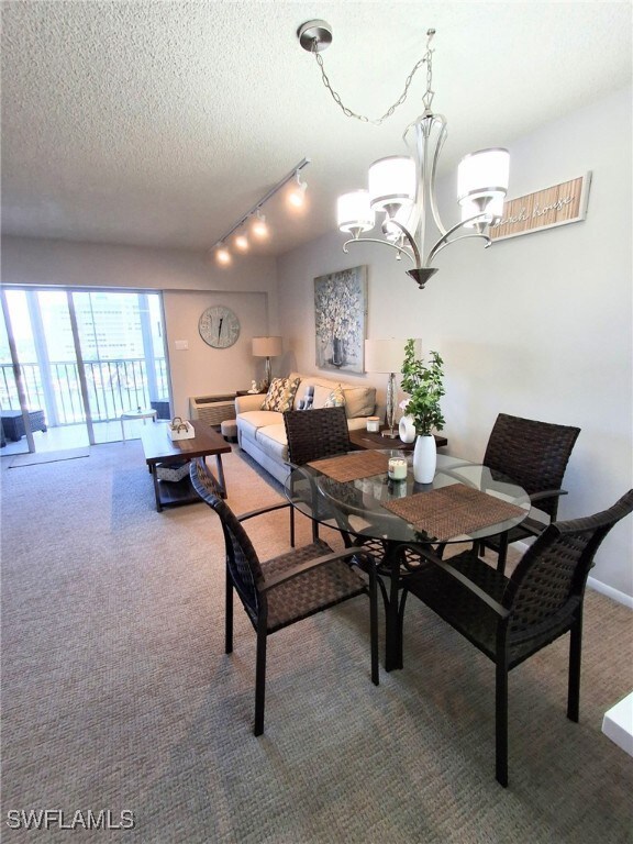 Carpeted dining room featuring a chandelier, rail lighting, and a textured ceiling