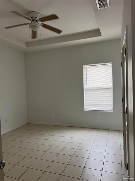 Unfurnished room featuring a raised ceiling, ceiling fan, and light tile patterned flooring