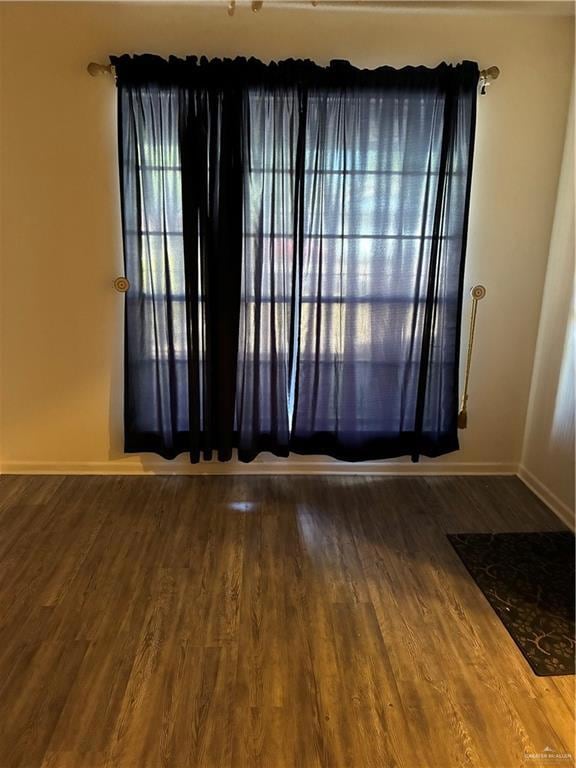 Spare room featuring dark wood-style flooring and baseboards
