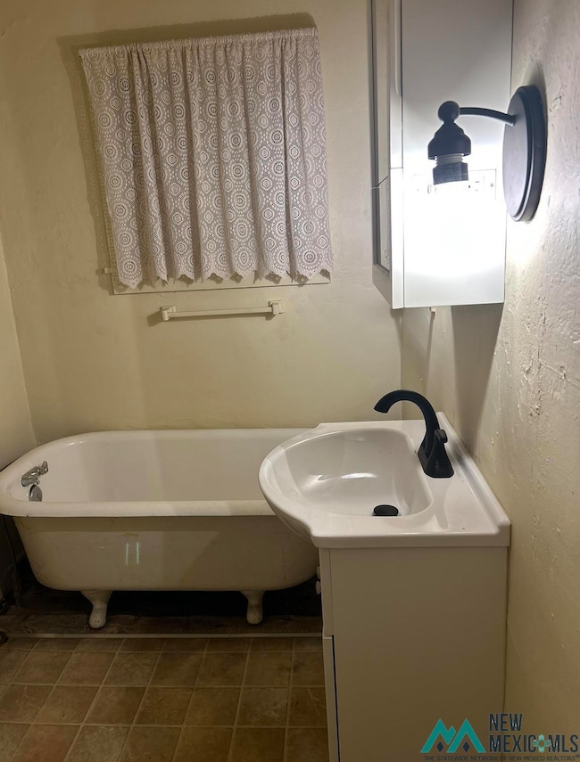Full bathroom with a freestanding bath, vanity, dark tile patterned flooring, and a textured wall