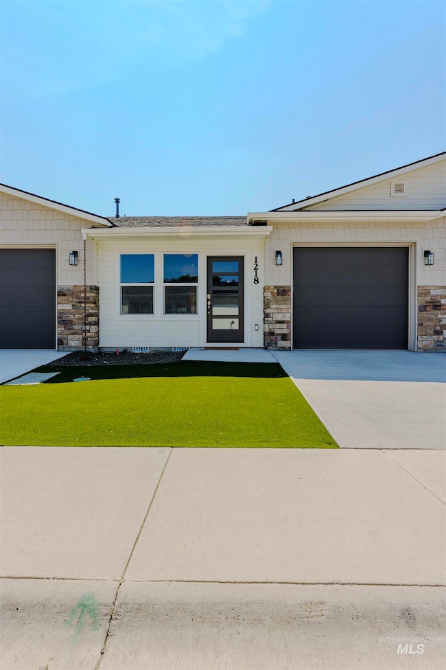 View of front of property featuring stone siding, concrete driveway, a front lawn, and an attached garage