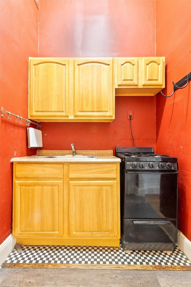 Kitchen featuring light brown cabinetry, black gas range oven, and baseboards
