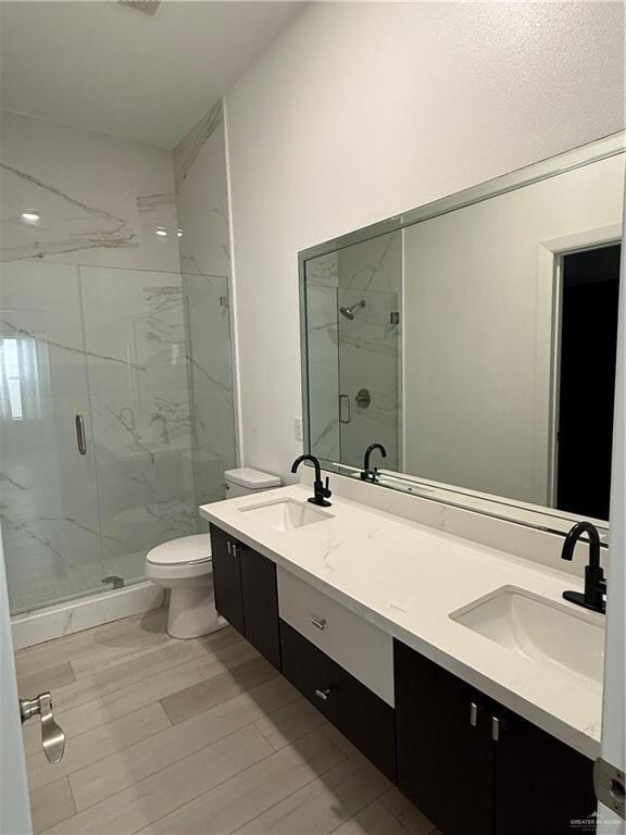 Bathroom with hardwood / wood-style flooring, double vanities and a shower with glass shower door