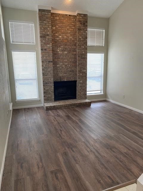 Unfurnished living room featuring a fireplace, dark wood finished floors, and a textured ceiling