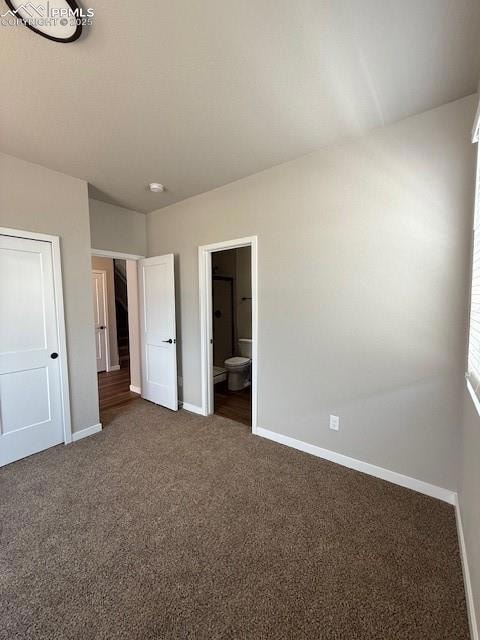 Unfurnished bedroom featuring dark carpet, connected bathroom, and a textured ceiling